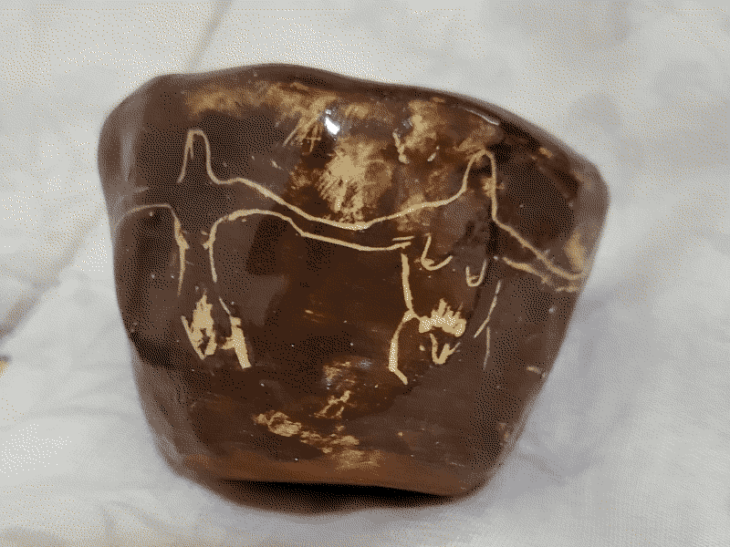 small ceramic cup, side view. abstracted transexuals, nude with arms interlocked, over dark brown slipware